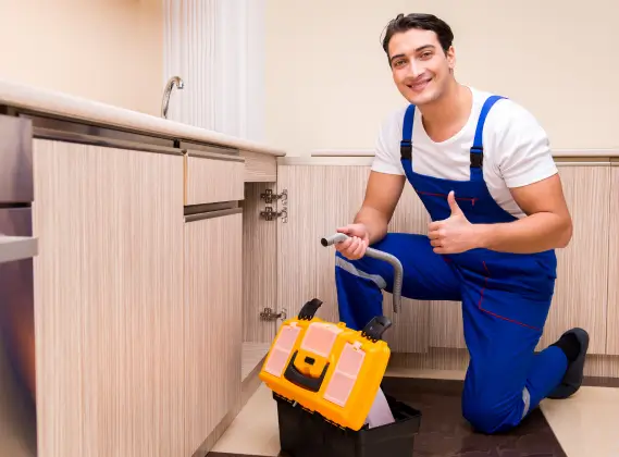 Smiling plumber fixing kitchen sink.